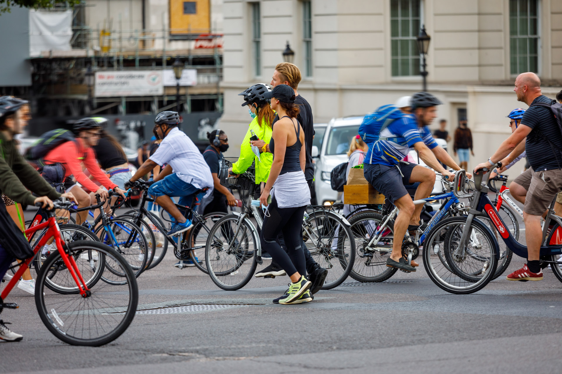 A large group of people on bikes cross a city junction in both directions